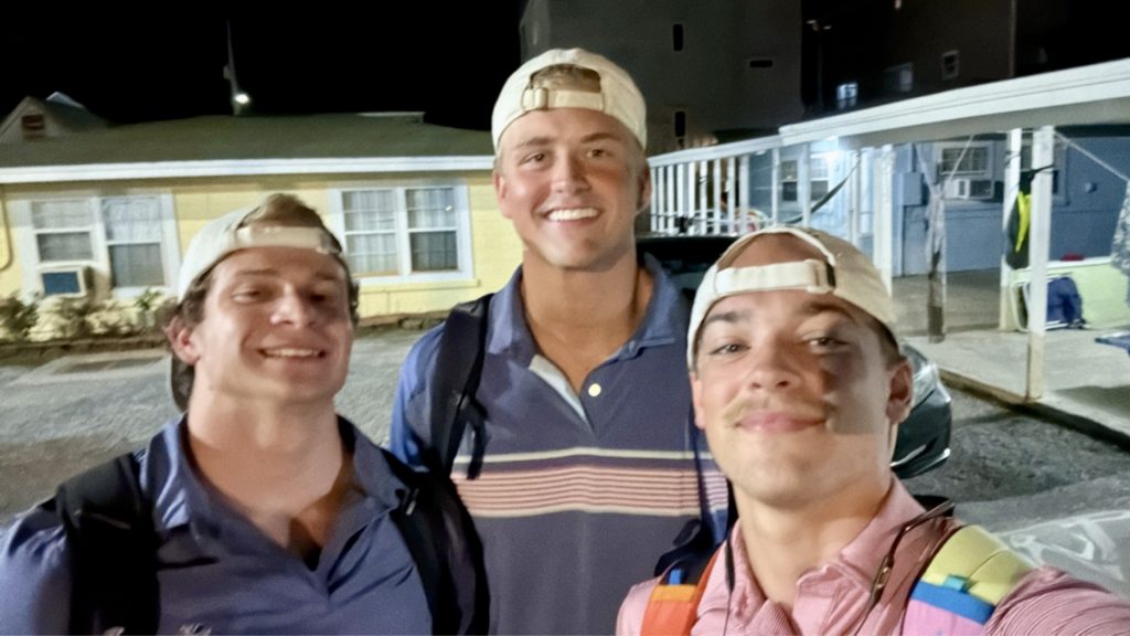 Three college males wearing backward caps smile in a group photo on Summer Beach Project